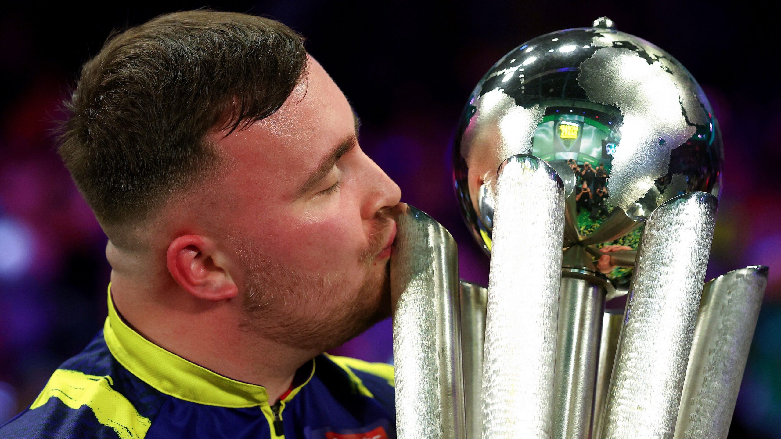 Luke Littler met een grote dartstrofee op het podium